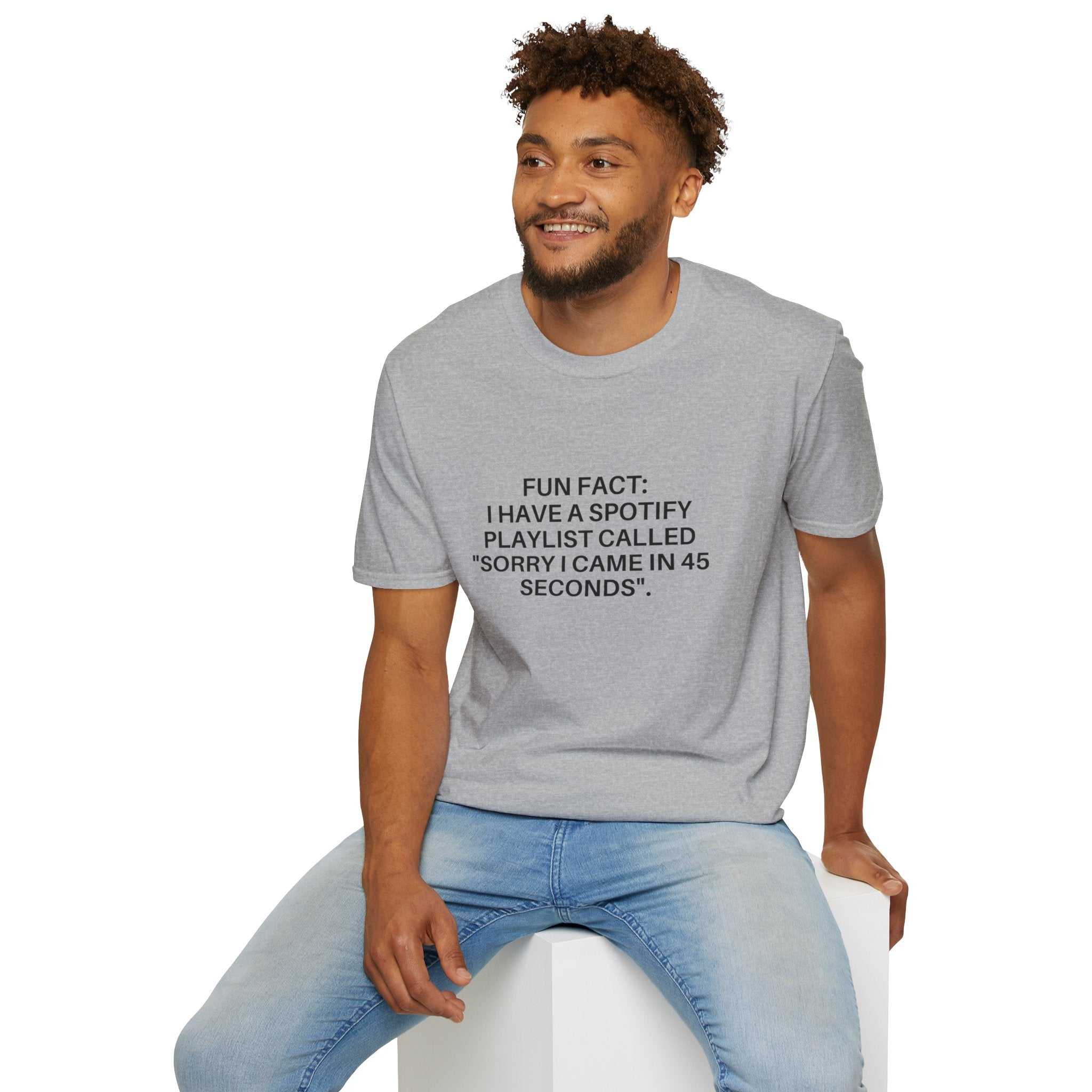 Man wearing light grey crew-neck tee with humorous black text print sitting on a white block